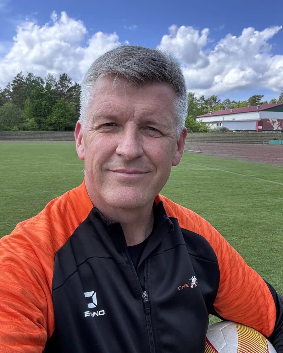Michael Otte auf dem Sportplatz, im Trainingsanzug der One on One Fußballschule, einen Ball unter dem Arm